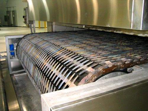 The oven's open grid conveyor allows air to circulate at high temperatures within the baking chamber.